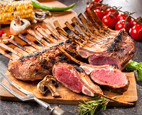 Cooked Rack of Lamb on cutting board surrounded by vegetables