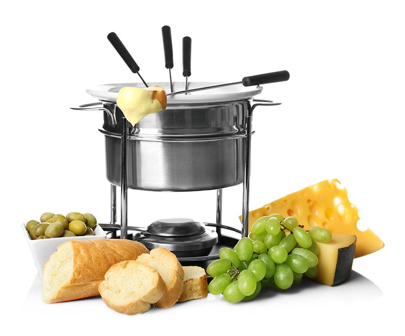 Cheese fondue in pot surrounded by bread, grapes, and a cheese wedge