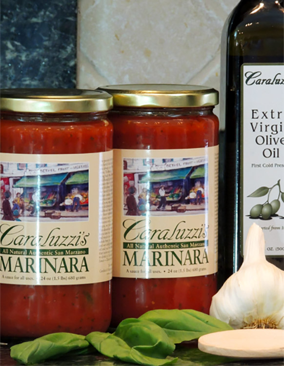 2 jars Caraluzzi's Marinara Sauce in kitchen with fresh garlic, basil leave, and Caraluzzi's Extra Virgin Olive Oil